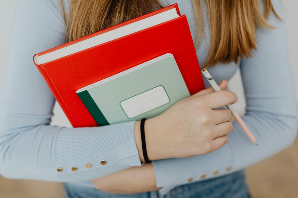 A close-up of a young student holding notebooks and a pencil, representing education and learning.